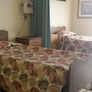 A hospital room with two twin beds adorned with floral bedspreads, separated by a curtain and a nightstand.