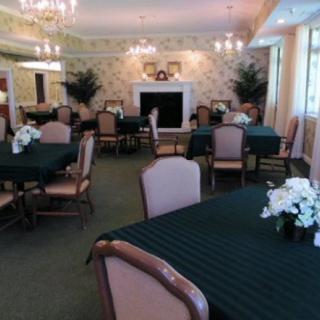 An elegant dining room with neatly arranged tables and chairs, illuminated by chandeliers and decorated with floral arrangements.