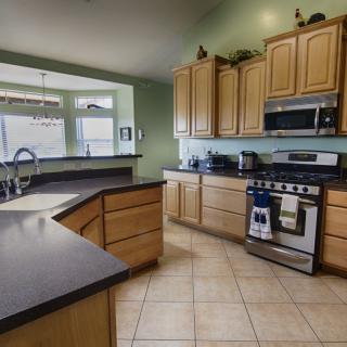 A modern kitchen interior featuring light wood cabinets, dark countertops, and stainless steel appliances.