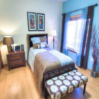 A cozy bedroom with modern decor, featuring a single bed, side table, lamp, and large window.