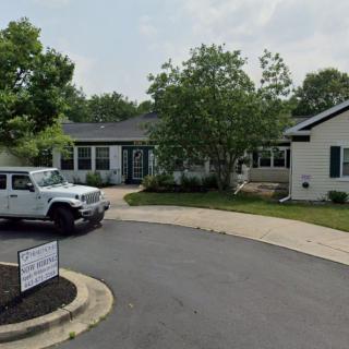 A suburban house with a driveway, a white car parked in front, and trees surrounding the yard.