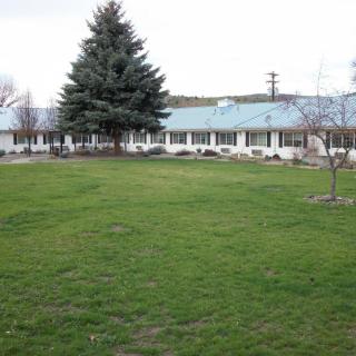 A building with a lawn and large tree in front, under a cloudy sky.