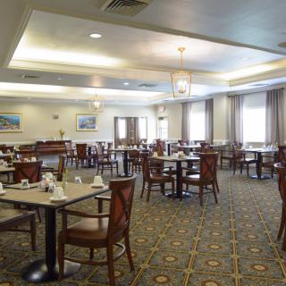A spacious and elegantly decorated dining room with multiple tables and chairs, well-lit by overhead lighting.
