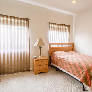 A simple bedroom with a single bed, nightstand, and lamp by the window.