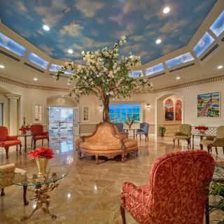 A beautifully decorated lobby with an artificial tree centerpiece and elegant seating arrangements, featuring a sky-themed ceiling mural.