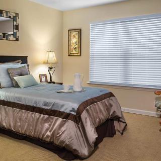 A cozy bedroom with a neatly made bed, soft lighting, and a large window.