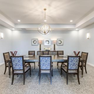 A spacious dining room with a large table and elegant chairs, featuring a modern chandelier and wall decorations.