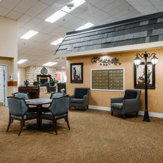 A cozy interior space featuring a seating area with chairs and a table, decorated with wall art and illuminated by indoor lighting.