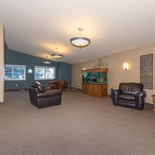 A spacious living room featuring leather chairs, an aquarium, and ceiling lights, with a cozy seating area on a carpeted floor.