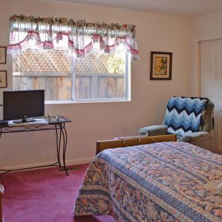 Cozy bedroom with a TV, armchair, and a patterned quilt on the bed.