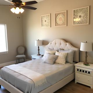 A cozy bedroom with neutral tones, featuring a tufted bed, white nightstands, decorative lamps, and wall art.