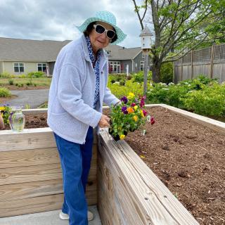 An elderly person tending to flowers in a raised garden bed on a cloudy day.