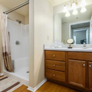 A cozy bathroom with a shower, wooden vanity, and large mirror.