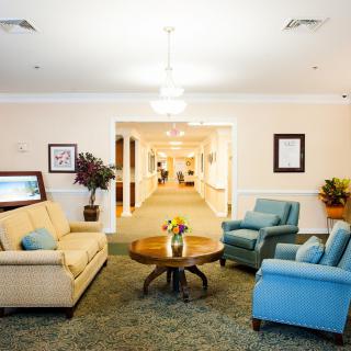 A cozy living area with sofas, armchairs, and a table, leading to a brightly lit hallway.