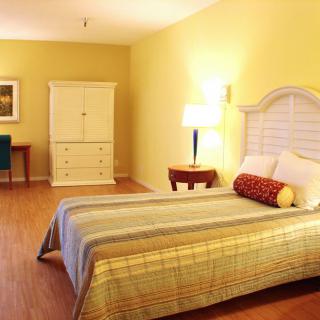 A cozy bedroom with warm yellow walls, featuring a bed, dresser, and side table with a lamp.