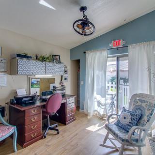 A cozy home office with a desk, computer, and comfortable seating, featuring natural light from a large window.
