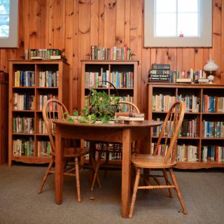 A cozy library corner with a wooden table and chairs surrounded by bookshelves filled with books.