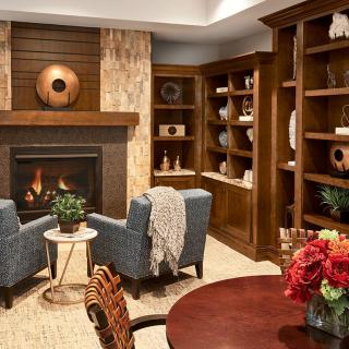 A cozy living room with a fireplace, armchairs, and bookshelves adorned with decor.