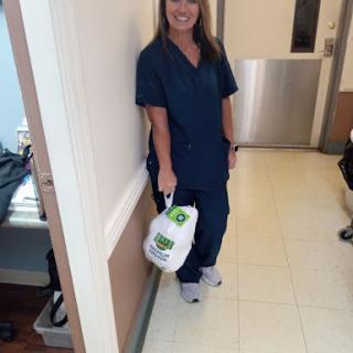 A healthcare professional in scrubs smiling while holding a bag.