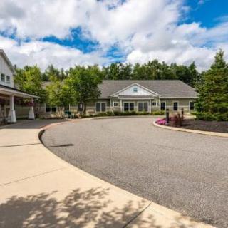 A scenic view of a building with a circular driveway, surrounded by trees and a partly cloudy sky.