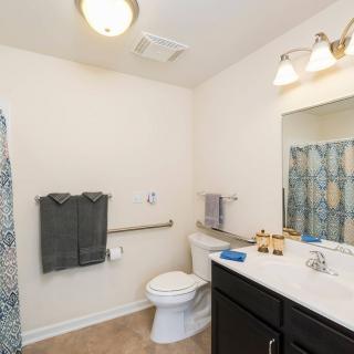 A modern bathroom with a shower, toilet, and sink area featuring towels and lighting.