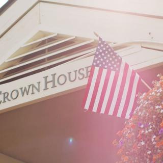 An American flag waves proudly in the sunlight outside a building marked 'Crown House'.