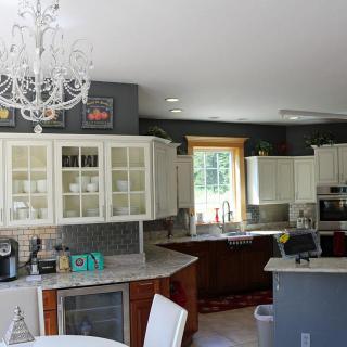 A modern kitchen with white cabinets, elegant chandelier, and ample natural light.