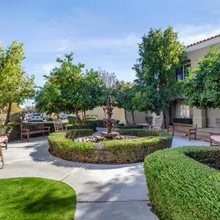 A beautifully landscaped courtyard with manicured shrubs, trees, and benches along a winding pathway.