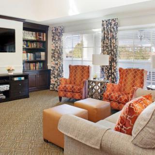 A cozy living room with vibrant orange accents, featuring a comfortable sofa, armchairs, a television, and a well-stocked bookshelf.