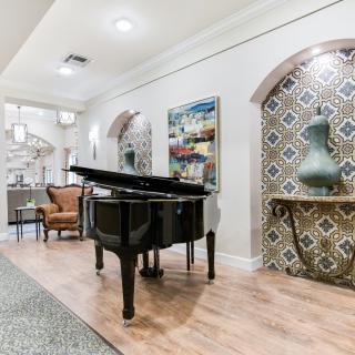 A stylish living room featuring a grand piano, elegant artwork, and a decorative vase on a console table.