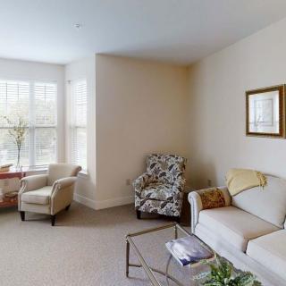A cozy living room with ample natural light, featuring a sofa and armchairs arranged around a glass coffee table.