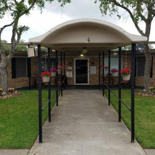 A welcoming entrance to a residential building, featuring a landscaped front area and an awning.
