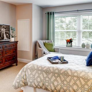 A cozy bedroom with a neatly made bed, a dresser, and ample natural light coming through the window.