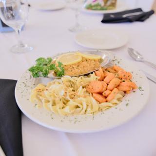 A beautifully arranged plate featuring fettuccine pasta, grilled salmon, cornbread, and a side of green salad.
