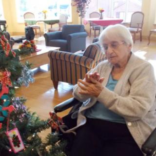 An elderly woman sitting in a wheelchair next to a decorated Christmas tree.