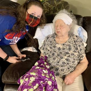 A caregiver attends to an elderly woman in a cozy living room setting.