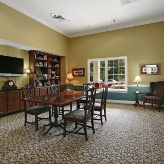A cozy living room with a table and chairs, bookshelf, television, and lamps.