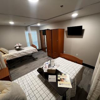 A spacious hospital room equipped with two beds, a wardrobe, and a television.