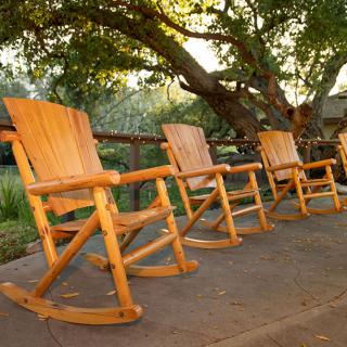 Four wooden rocking chairs on a patio overlooking a garden at sunset.