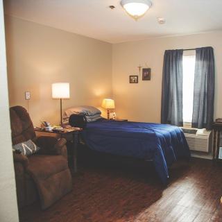A cozy bedroom with a bed, lamp, recliner chair, and window with curtains.
