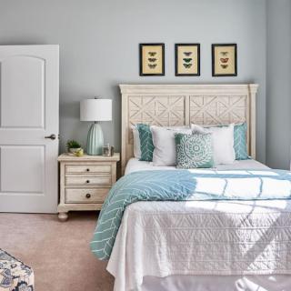 A cozy bedroom with elegant decor, featuring a neatly made bed with blue and white bedding, a nightstand with a lamp, and framed artwork on the wall.