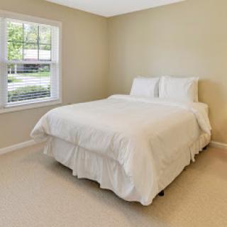 A bright and minimalistic bedroom showcasing a neatly made bed with white bedding and a window allowing natural light in.