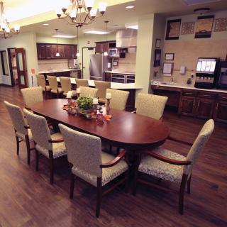 A spacious dining room area with a wooden table and upholstered chairs, adjacent to an open kitchen, featuring chandeliers and wood flooring.