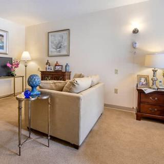 A cozy living room with a beige sofa, decorated with a lamp, side table, and artwork on the walls.