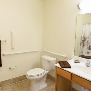 A clean and accessible bathroom with grab bars, a toilet, a sink with a vanity, and a mirror.