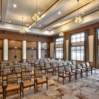 A well-lit conference room set up with rows of chairs, featuring elegant wood paneling and modern lighting.