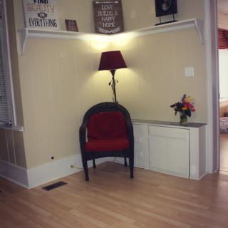 A cozy corner with a red chair, lamp, and decorative shelves.