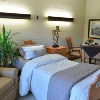 A well-furnished hospital room with a comfortable bed, chairs, and decorative elements.