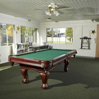 A spacious game room featuring a classic pool table under a ceiling fan, with natural light streaming in from large windows.