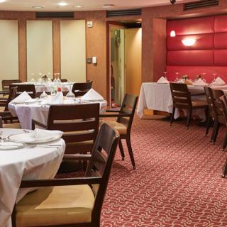 A cozy restaurant dining area with neatly arranged tables and chairs, featuring white tablecloths and red accents on the walls.
